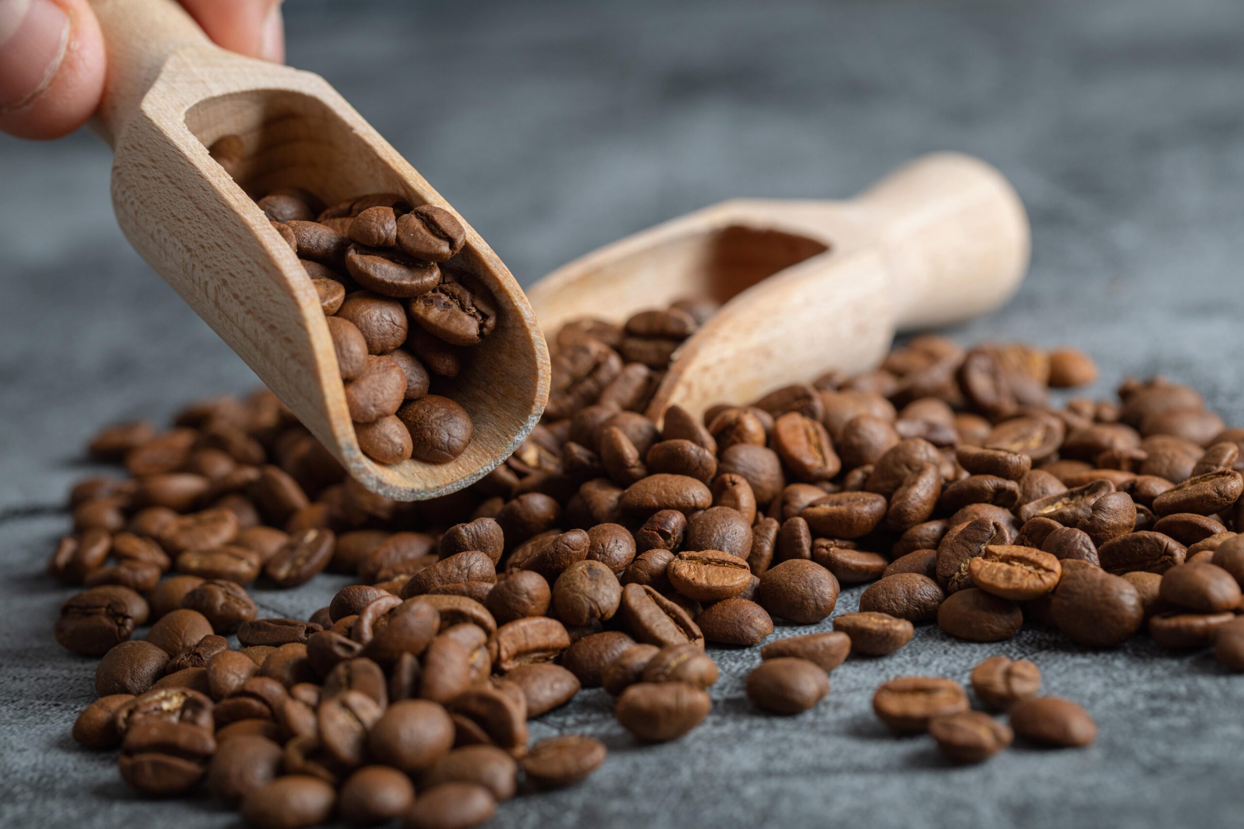 male-hand-holding-wooden-spoon-aromatic-coffee-beans-marble-background-min